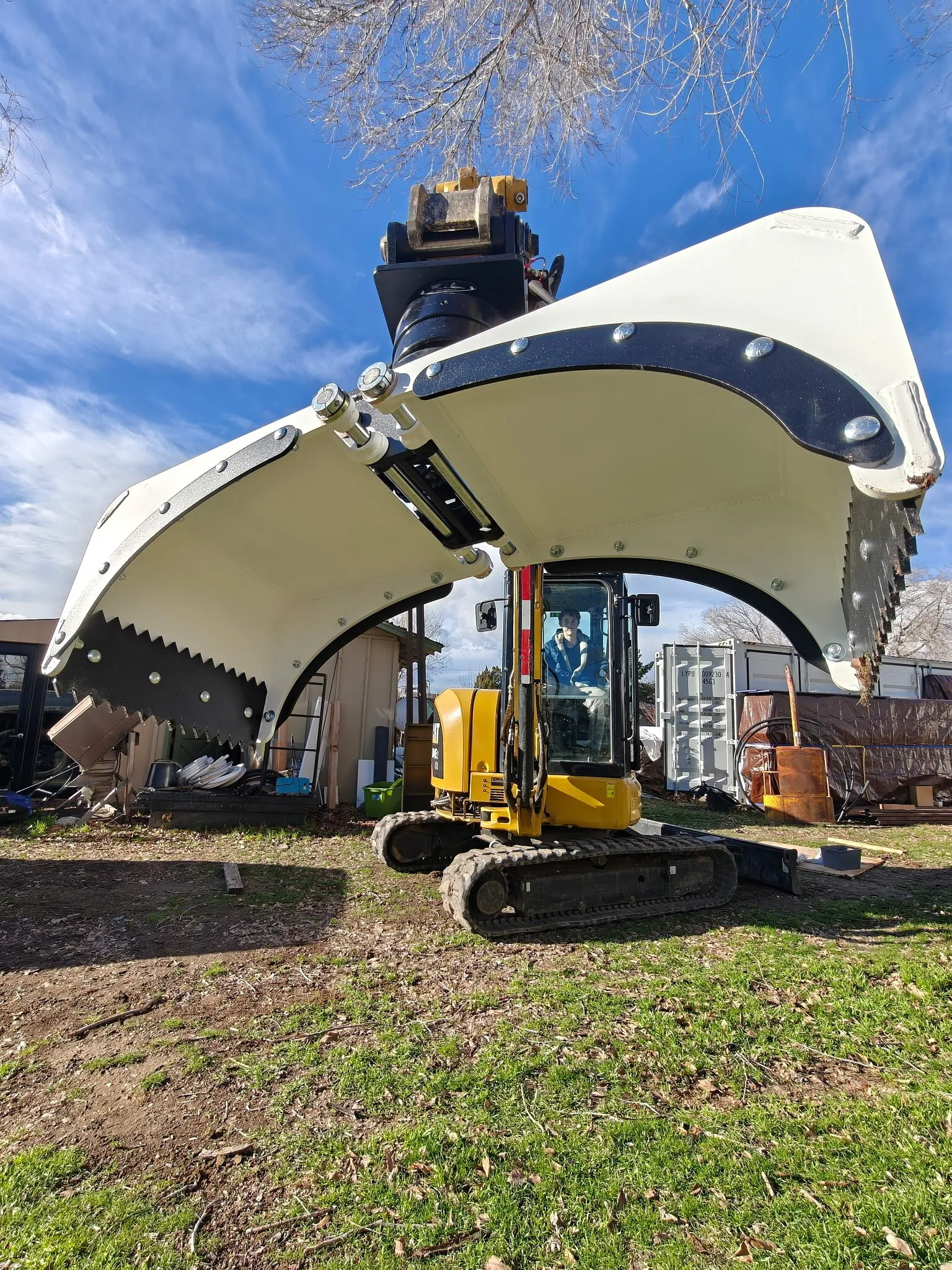 Excavator bucket and thumb attachment powder coated white, fitted to a mini excavator outdoors