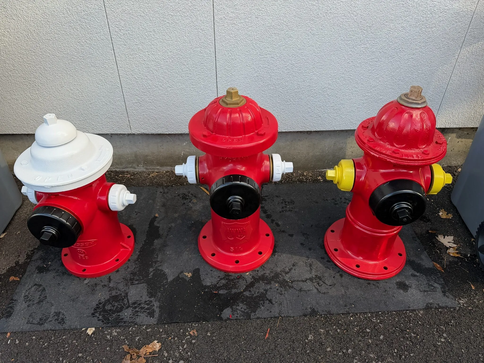 Three fire hydrants powder coated red, one with a white top and one with yellow caps