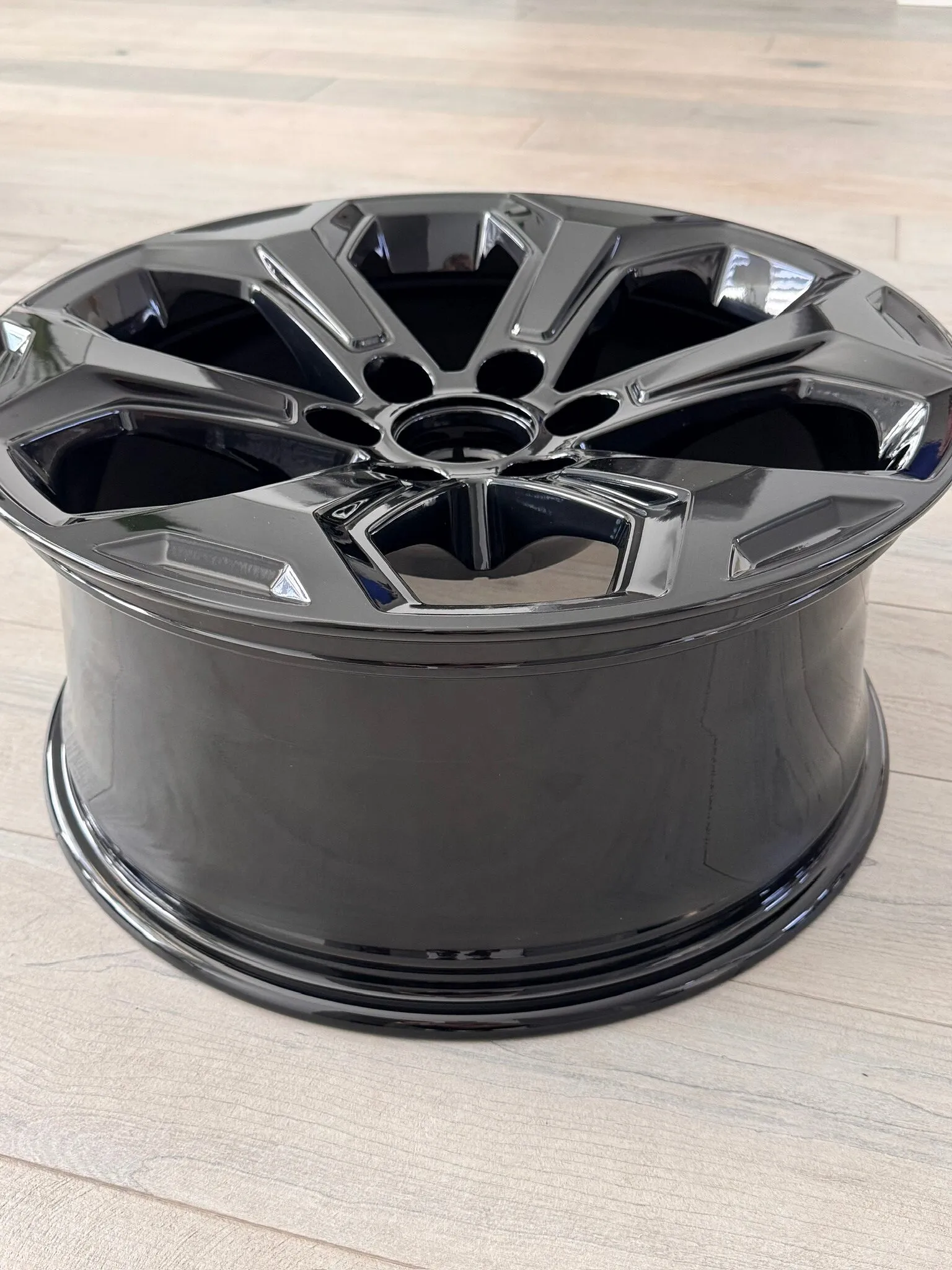 Gloss black powder-coated wheel on a wood floor, seen at an angle to show the barrel