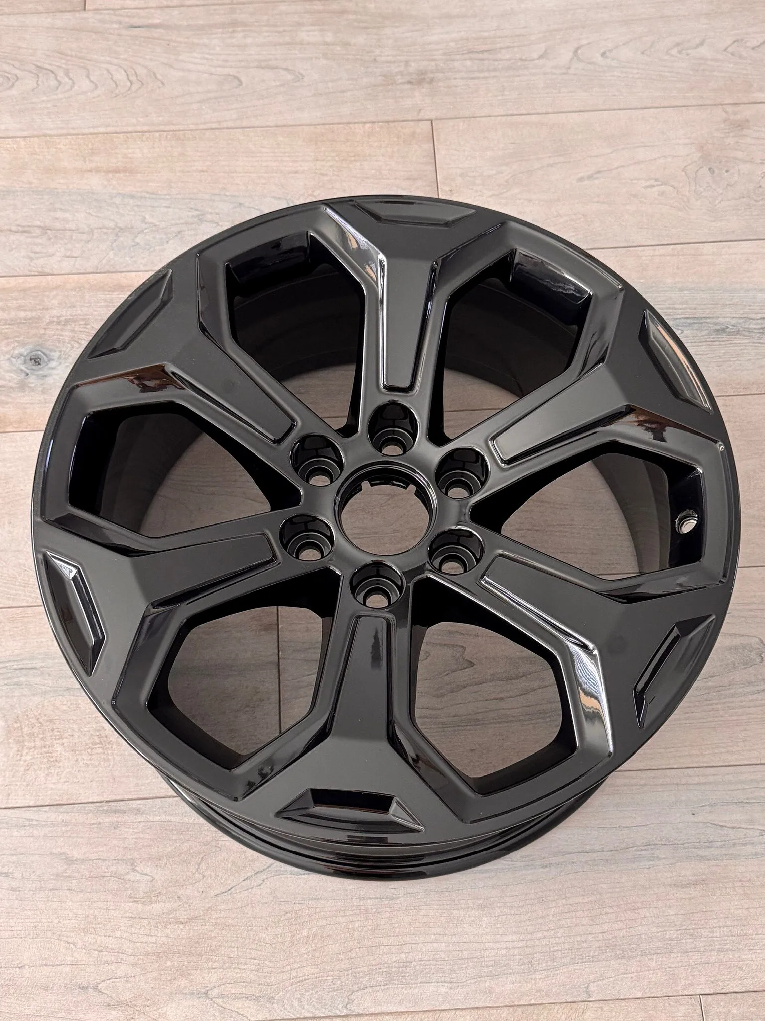 Gloss black powder-coated wheel lying on a wood floor, seen from above