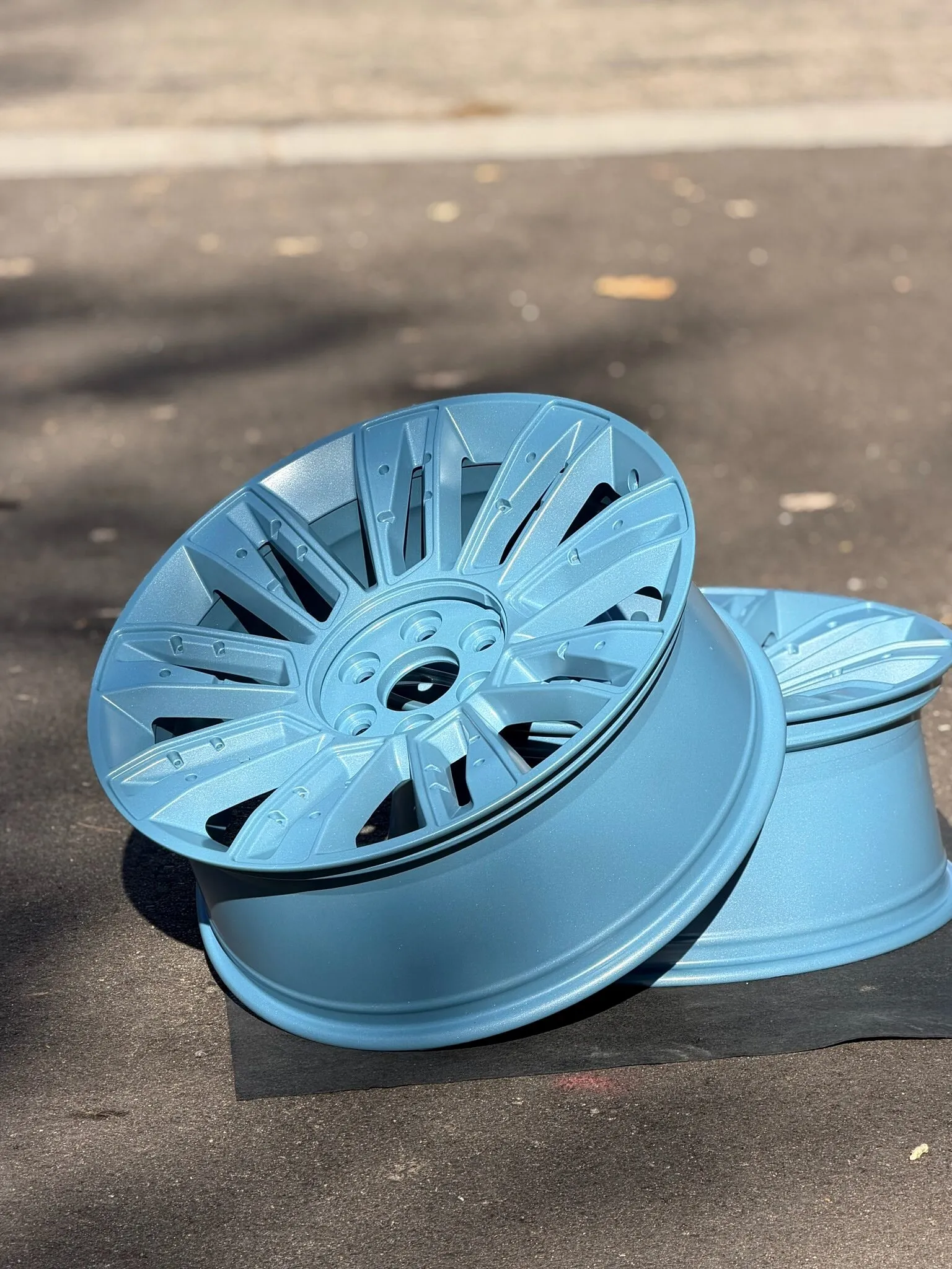 Light blue powder-coated wheel leaning on its pair, outdoors